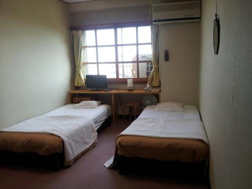 two beds in a room with a desk and a computer at Orange Pension in Gamagori