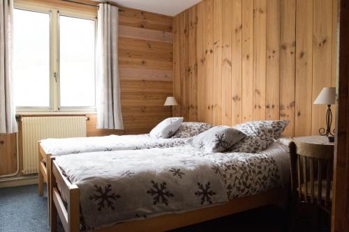 two beds in a room with wooden walls and windows at Les Agneaux in Villar-dʼArène