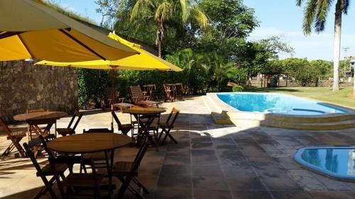 un patio con mesas y sombrillas junto a una piscina en Hotel Caiçara Bistrô e Eventos Ltda, en Itaperuna