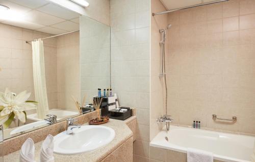 een badkamer met een wastafel, een bad en een spiegel bij ZiQoo Hotel Apartments Dubai in Dubai