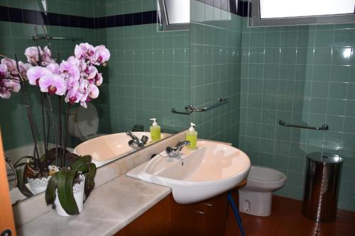 a bathroom with a sink and a toilet and pink flowers at Caloura Camellia House in Caloura