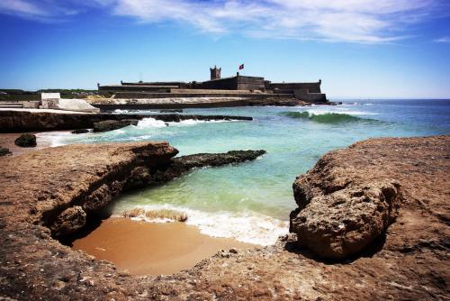 a beach with rocks and the ocean and a lighthouse at Carcavelos Beach Apartment in Cascais