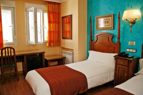 a hotel room with two beds and a desk and windows at Hostal Victoria II in Madrid