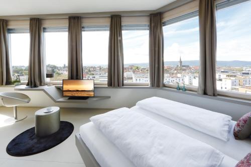 a bedroom with a bed and a desk and windows at aquaTurm Hotel & Energie in Radolfzell am Bodensee