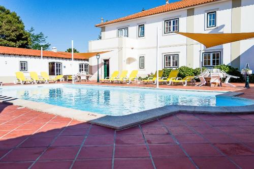 a pool in front of a building with chairs and an umbrella at Casa Da Padeira - Turismo Rural in Alcobaça