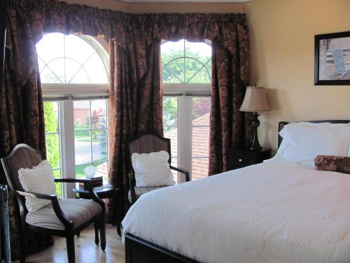 a bedroom with a bed and two chairs and windows at Arnica Bed & Breakfast in Niagara on the Lake