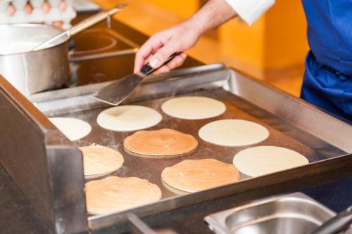 a person cooking pancakes on a grill with a spatula at Hotel Mediterraneo in Benidorm