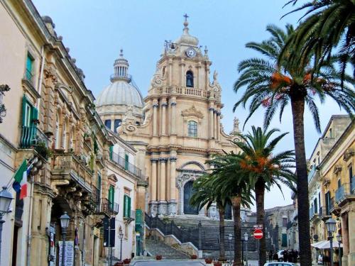 a building with a clock tower and palm trees at Mario Leggio Apartment in Ragusa