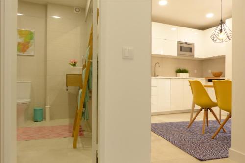 a kitchen and dining room with yellow chairs and white cabinets at Palhas apartment in Ericeira