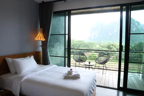 a bedroom with a bed and a balcony with chairs at Inthira Vangvieng in Vang Vieng