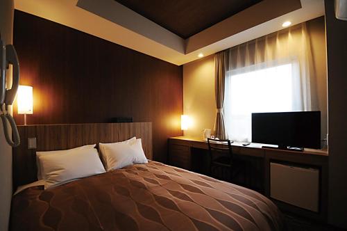 a bedroom with a bed and a desk and a television at Hotel Lexton Tanegashima in Nishinoomote