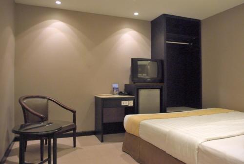 um quarto com uma cama, uma televisão e uma cadeira em Hotel Gajahmada Pontianak em Pontianak