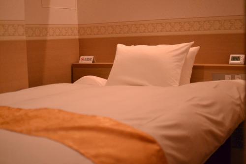 um quarto com uma cama com lençóis brancos e uma almofada em Hotel Boti Boti em Osaka