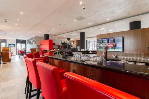 a restaurant with red chairs and a bar at Bastion Hotel Eindhoven Waalre in Eindhoven