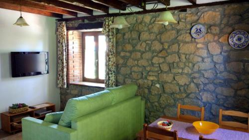 sala de estar con sofá verde y pared de piedra en Apartamentos La Huertona, en Queveda