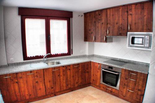 een keuken met houten kasten, een wastafel en een magnetron bij Casa Rural Ca'l Gonzalo in Almazán