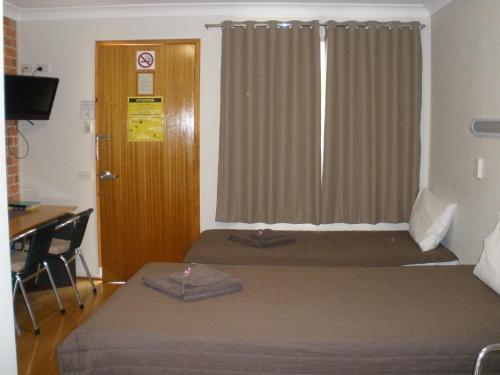 a bedroom with two beds and a desk and a window at Palms Oasis Motel in Coopernook
