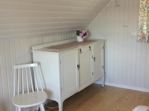 a white cabinet with a chair and a vase of flowers at Vimmerby Lilla utsikten in Tuna