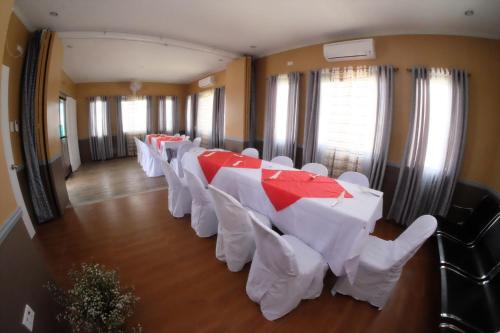 a row of tables and white chairs in a room at L & M Hearthstones Lodge in Oslob