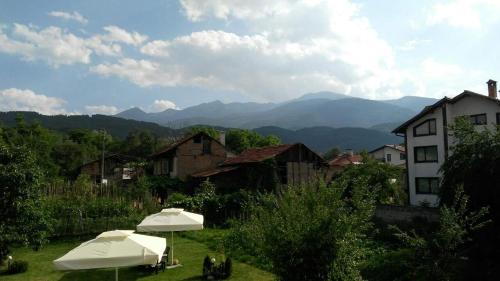 two white umbrellas in a village with mountains in the background at Guest House Raffe in Dobrinishte