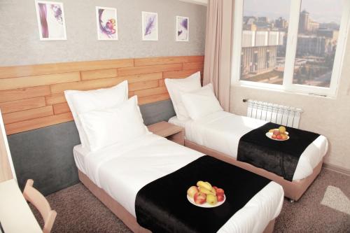 two beds in a hotel room with fruit on plates at Small Hotel in Bishkek