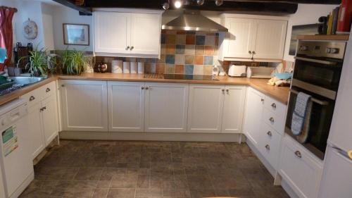 a kitchen with white cabinets and tile floors at TopHeavy Cottage Mevagissey in Mevagissey