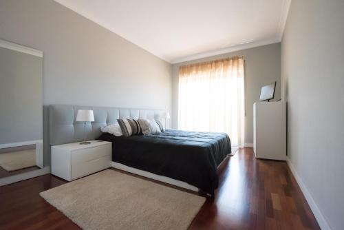 a white bedroom with a bed and a window at Apartamento Mouzinho de Albuquerque in Matosinhos