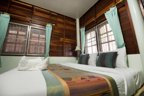 two beds in a room with two windows at Pongphen Guesthouse - SHA Plus Certified in Kanchanaburi