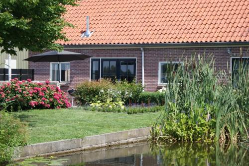 a house with an umbrella next to a pond at Gastenverblijf De Natureluur in Noorden