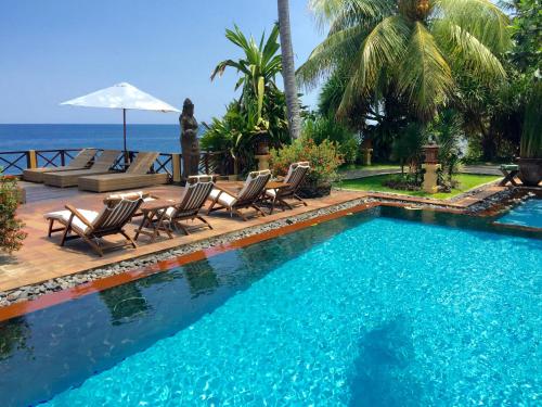 a swimming pool with chairs and the ocean in the background at Villa Boreh Beach Resort and Spa in Tejakula