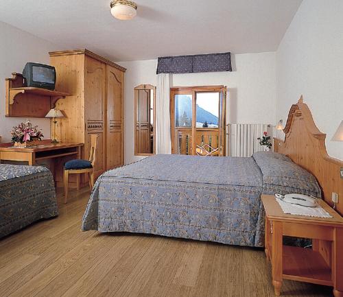 Schlafzimmer mit einem Bett, einem Schreibtisch und einem TV in der Unterkunft Hotel Jolanda in San Martino di Castrozza