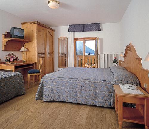 een slaapkamer met een bed, een bureau en een televisie bij Hotel Jolanda in San Martino di Castrozza