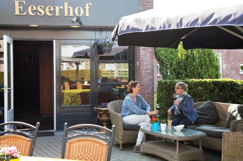 two women sitting on a patio under an umbrella at Hotel Restaurant Eeserhof in Ees