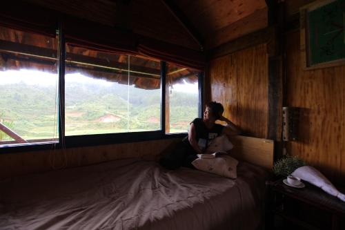 a woman sitting on a bed in a room with a window at Mu Cang Chai Eco Lodge in Nam San