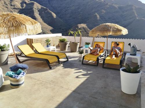 two people sitting in chairs and umbrellas on a patio at Vilna House with private pool, jacuzzi and garden -Optional pool and jacuzzi heating in Agaete