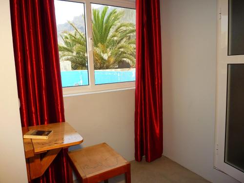 Habitación con cortinas rojas, mesa y ventana en kasa Tambla, en Ponta do Sol