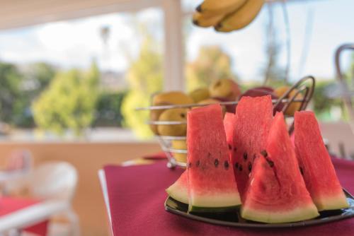 a plate of watermelon on a table with a basket of fruit at Hotel Flora in Noto