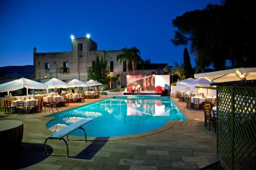 a swimming pool with tables and chairs in front of a building at Agriturismo Baglio Fontana in Buseto Palizzolo