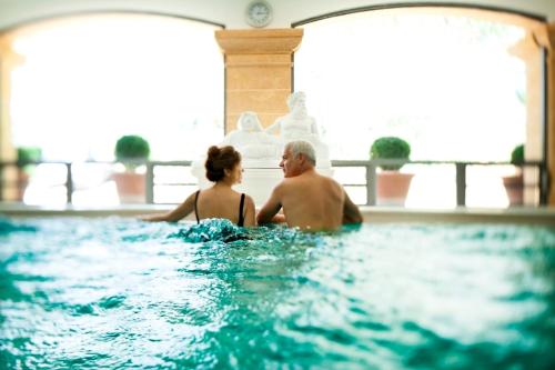 un hombre y una mujer sentados en una piscina en Résidence les Grands Pins, en Gréoux-les-Bains