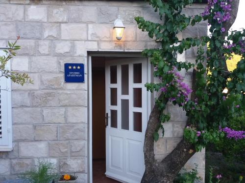 une porte blanche menant à un bâtiment en pierre avec des fleurs violettes dans l'établissement Apartman Matić, à Ston