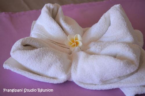 a white towel with a flower on top of it at Frangipani Studio Réunion in La Saline les Bains