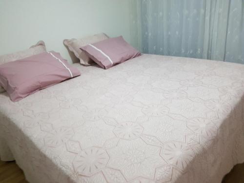 Cama grande con sábanas y almohadas rosas y blancas en Apartamento Barra Paraíso Tropical, en Río de Janeiro