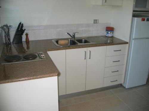 a kitchen with white cabinets and a sink and a refrigerator at Harriet Place apartment in Darwin