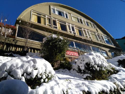 un edificio cubierto de nieve con arbustos delante de él en Moving Hostel Travel Bar en San Carlos de Bariloche