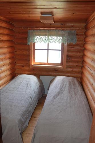 two beds in a log cabin with a window at Keitaanniemen lomamökki in Haapamäki