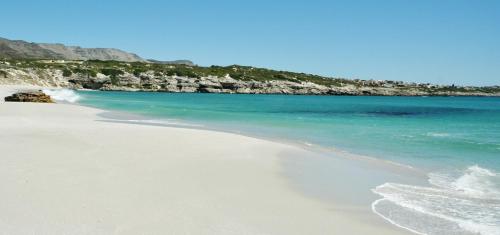 a sandy beach with the ocean and mountains in the background at Kleinzee Oceanfront Guesthouse in Gansbaai