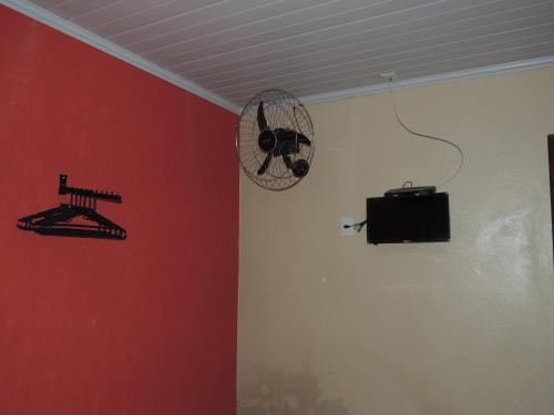 a room with a red wall with a fan and a television at Pousada Centaurus in Alto Paraíso de Goiás
