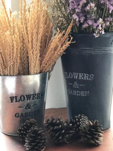 two buckets with flowers and gardens written on them next to pine cones at De Nan Hotel in Nan