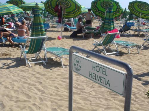 a hotel hawaii sign on a beach with chairs and umbrellas at Hotel Helvetia in Lido di Jesolo