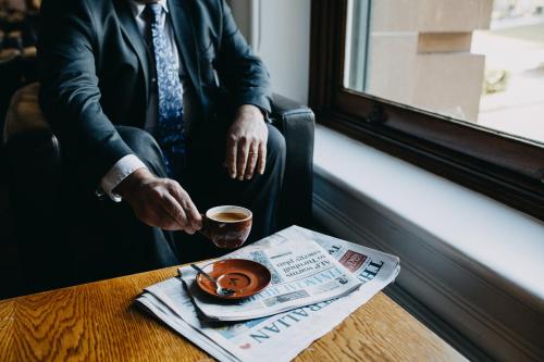 a man sitting at a table with a newspaper and a cup of coffee at Treasury Brisbane in Brisbane